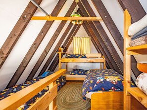 A cozy attic bedroom with a sloped ceiling, wooden bunk beds, a small table, and a patterned rug.