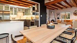 Une cuisine moderne avec des poutres en bois, un îlot central et un coin repas comprenant une grande table et des chaises.