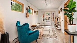 Une pièce avec un fauteuil turquoise, une décoration murale représentant une guitare, une grande plante en pot et un tapis à motifs.