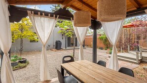 Une terrasse extérieure avec une table et des chaises en bois, recouverte d’un toit en bois et agrémentée de lampes suspendues.