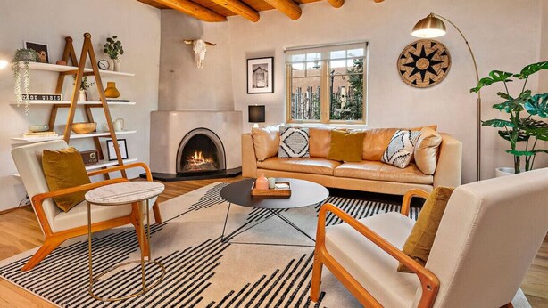 Un salon chaleureux avec une cheminée, des poutres apparentes en bois au plafond, un canapé avec des coussins, une table basse et une bibliothèque.