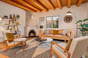 A cozy living room with a fireplace, wooden ceiling beams, a sofa with cushions, a coffee table, and a bookshelf. - High Design with Fabulous Patio (Santa Fe)