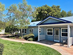 A two-story house with a blue roof and white trim, surrounded by a well-maintained lawn and trees.