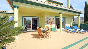 A covered outdoor dining area with a table and chairs, a mural on the wall, and a poolside lounge area with sun loungers. - Peaceful villa with heatable pool (Carvoeiro)