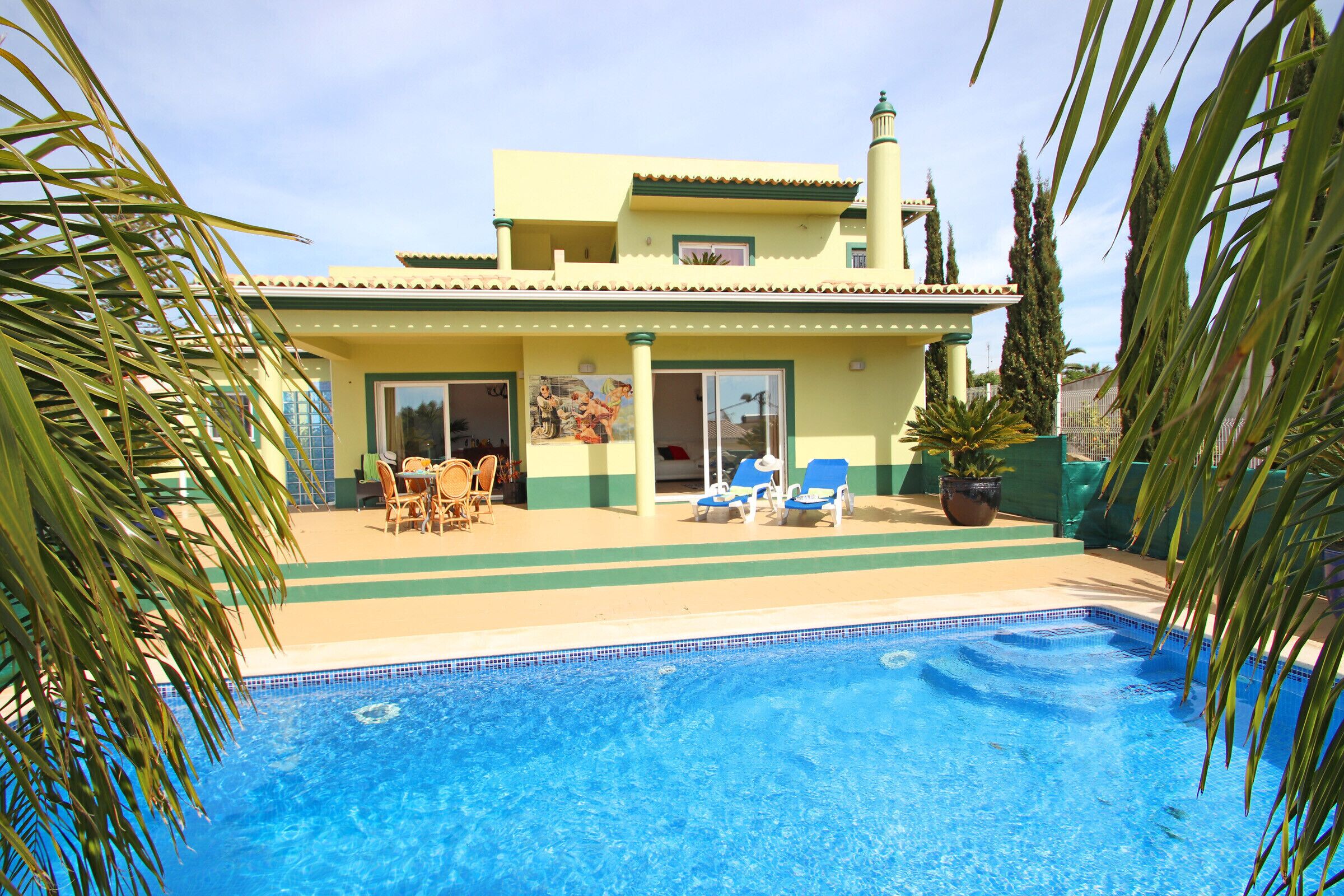A two-story building with a swimming pool, outdoor seating, and a garden.