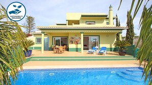 A yellow building with a swimming pool, outdoor seating, and palm trees. - Peaceful villa with heatable pool (Carvoeiro)