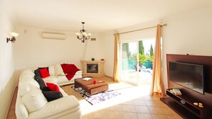 A living room with a sofa, coffee table, TV, fireplace, and a sliding glass door leading to a balcony. - Peaceful villa with heatable pool (Carvoeiro)