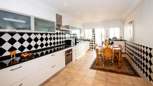 A modern kitchen with black and white checkered backsplash, white cabinets, and a dining area with a wooden table and chairs. - Peaceful villa with heatable pool (Carvoeiro)