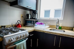 A kitchen with a gas stove, a coffee maker, a kettle, and a sink.