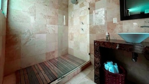 A bathroom with a glass-enclosed shower, a marble-tiled wall, a sink with a blue basin, and a mirror above the sink.