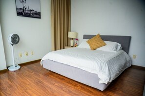 A hotel room with a bed, a standing fan, a lamp, and a wall-mounted picture.