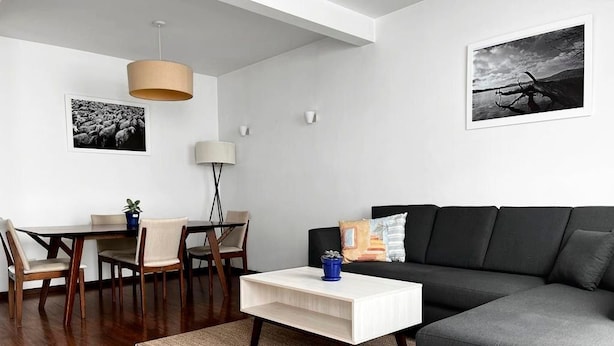 A modern living room with a dark grey sofa, a white coffee table, and a dining area with a wooden table and chairs.