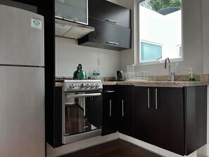 Une cuisine équipée d’un réfrigérateur en acier inoxydable, d’une cuisinière, de meubles de rangement noirs et d’une fenêtre laissant entrer la lumière naturelle.