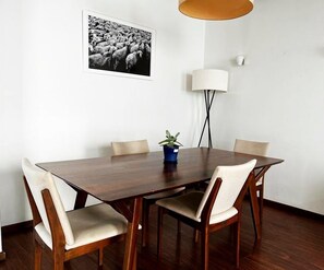 A dining area with a wooden table, four chairs, a potted plant, a wall-mounted lamp, and a framed picture.