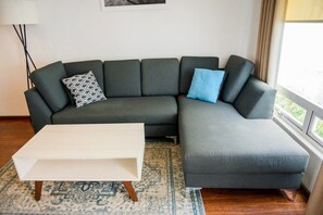 Un salon moderne avec un canapé d’angle gris, une table basse blanche et un tapis à motifs.