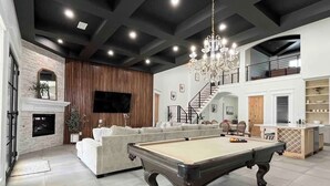 A spacious living area with a pool table, a fireplace, and a modern staircase.