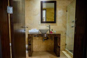 Un bagno con un mobile vanitario in marmo, un lavandino, uno specchio e una doccia.