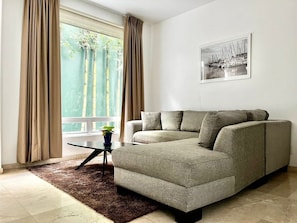 A living room with a sofa, a coffee table, a potted plant, and a window with curtains.