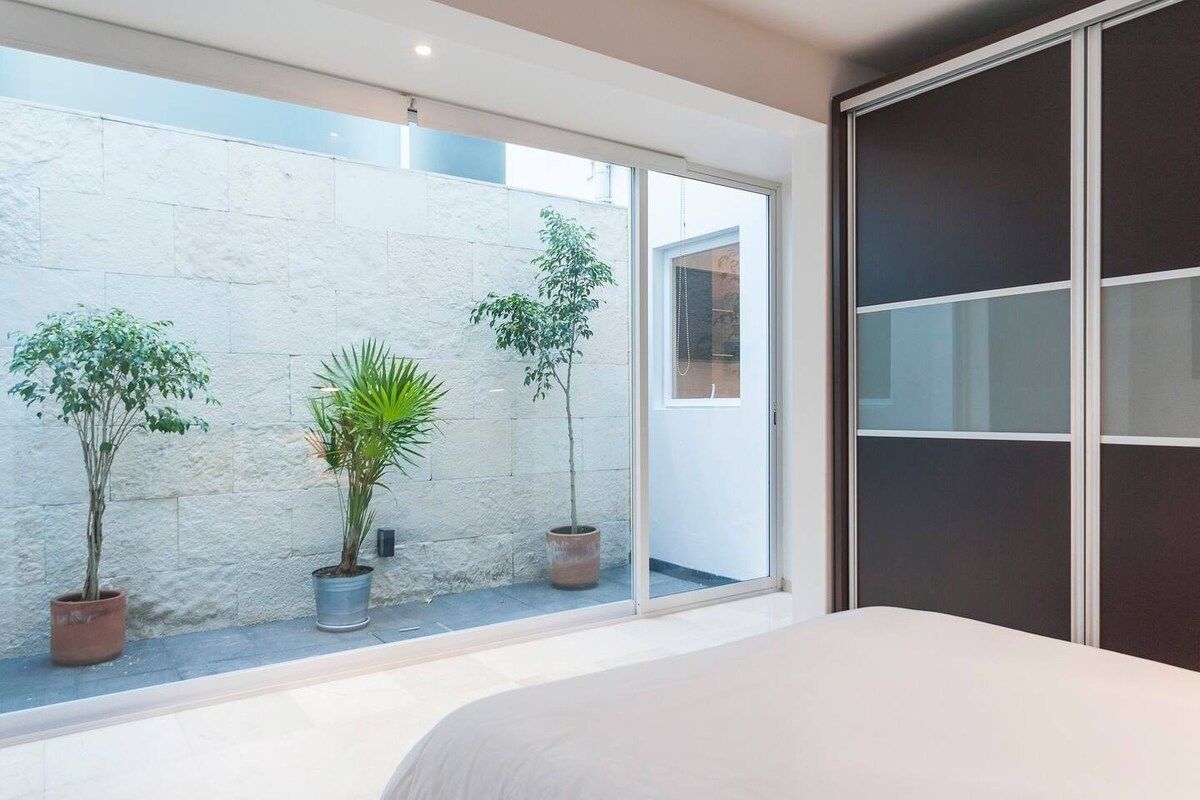 Een slaapkamer met een groot raam, een bed en potplanten.