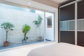 A bedroom with a large window, a bed, and potted plants.