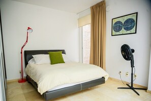 Un dormitorio con una cama, una lámpara de pie roja, un ventilador de pie negro y un mapa colgado en la pared.