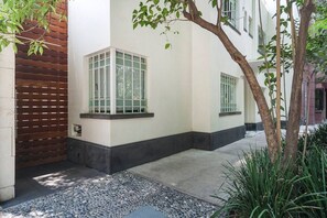 Un edificio con fachada blanca, una puerta de madera y un acceso pavimentado.