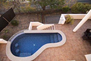 Une piscine à bord incurvé, entourée d’une terrasse en briques. Des marches permettent d’y descendre, et une rampe est visible.