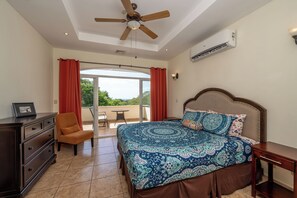 A bedroom with a bed, a dresser, a chair, a ceiling fan, and a view to the outside.
