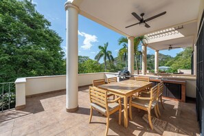 An outdoor patio with a table and chairs, a ceiling fan, and a grill.
