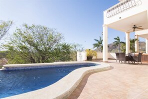 Une piscine à bord incurvé, entourée d’un patio aménagé avec des meubles d’extérieur et un espace salon abrité.