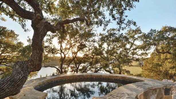 A stone pool with a waterfall, surrounded by trees and a clear sky. - Lake Travis Waterfront, Pool, Pool Table, Shuffleboard, Floating Boat Dock (Marble Falls)