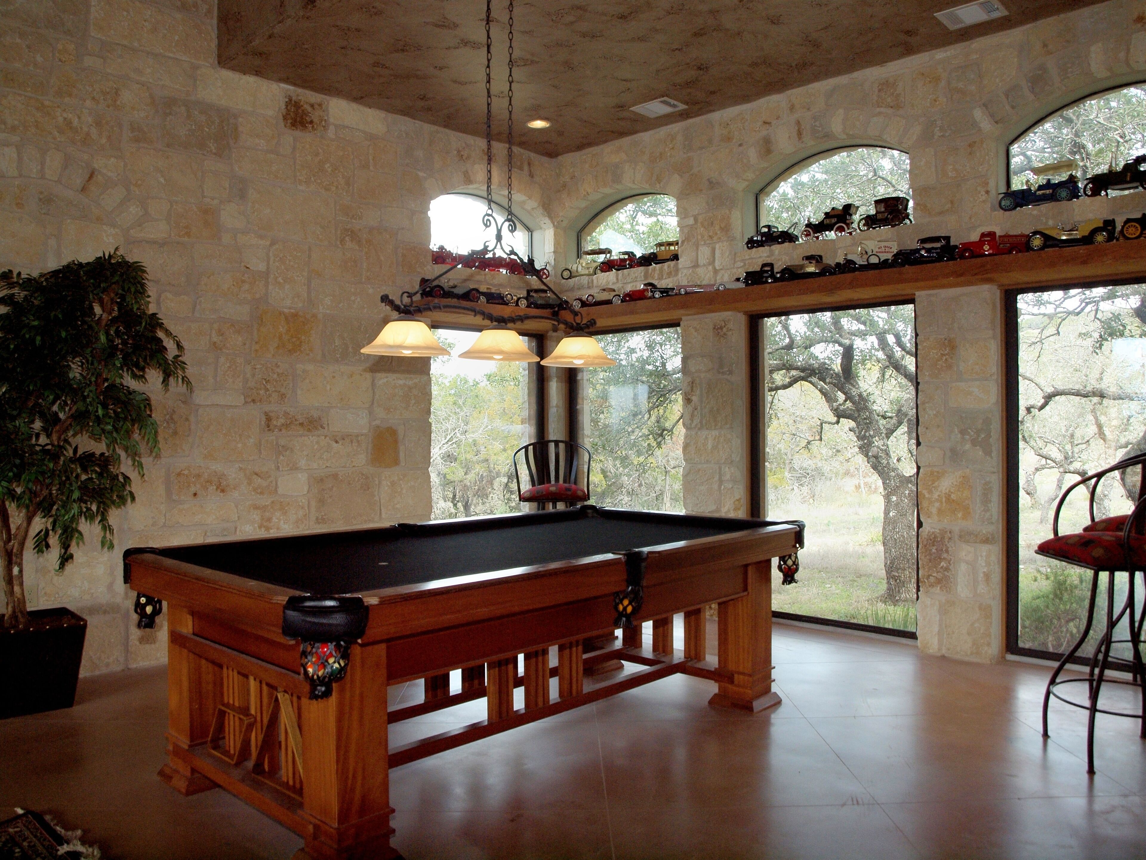 A pool table in a room with stone walls and large windows.