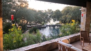 A patio with stone walls, a wooden bench, and a wooden chair overlooking a pond with a stone bridge. - Lake Travis Waterfront, Pool, Pool Table, Shuffleboard, Floating Boat Dock (Marble Falls)