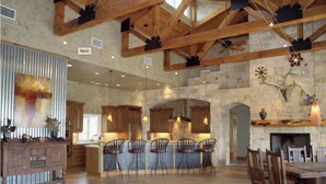A spacious kitchen with a stone wall, wooden beams, and a dining area with chairs and a table. - Lake Travis Waterfront, Pool, Pool Table, Shuffleboard, Floating Boat Dock (Marble Falls)