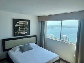 Une chambre d’hôtel avec un lit, une grande fenêtre donnant sur la ville et une œuvre d’art encadrée au mur.