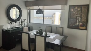 Un'area pranzo moderna con vista sulla città attraverso una grande finestra, uno specchio rotondo e un'opera d'arte incorniciata al muro.