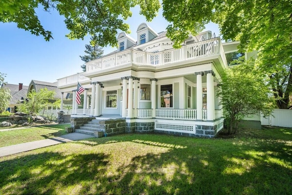 A two-story house with a front porch, a stone foundation, and a flag.