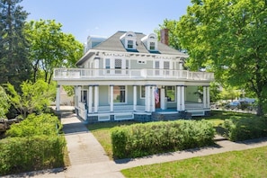 A two-story house with a porch, a chimney, and a flag.