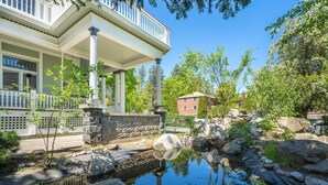 A building with a covered porch, a stone wall with an American flag, and a small pond with rocks and plants. - Entire 2nd and 3rd level of Spacious Historic Home (Spokane)