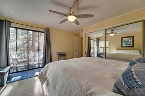 Ein Schlafzimmer mit einem großen Bett, einem Deckenventilator, einer Glastür zum Balkon und einem großen Spiegel.