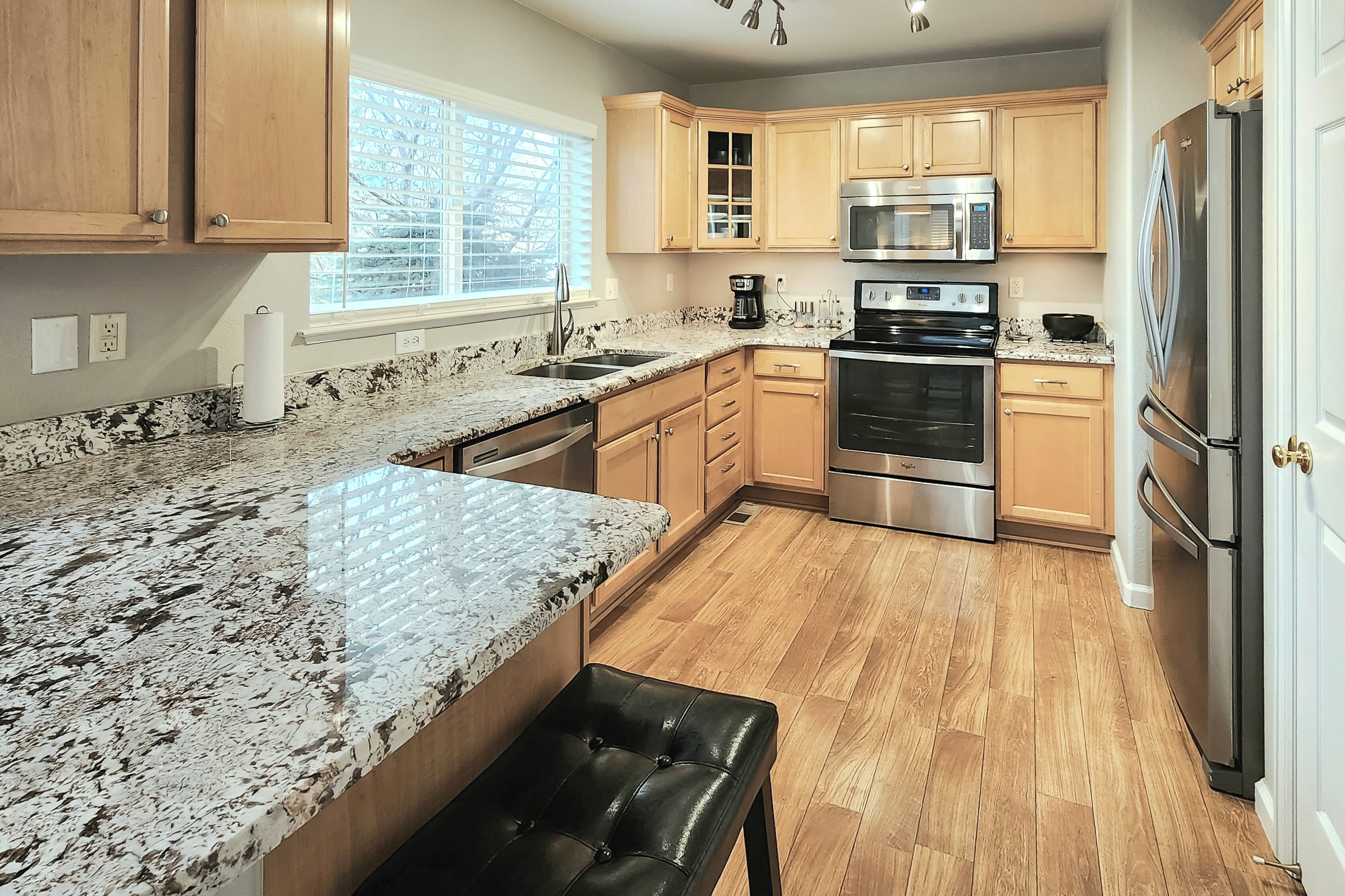 Una cocina moderna con encimeras de granito, electrodomésticos de acero inoxidable y armarios de madera.