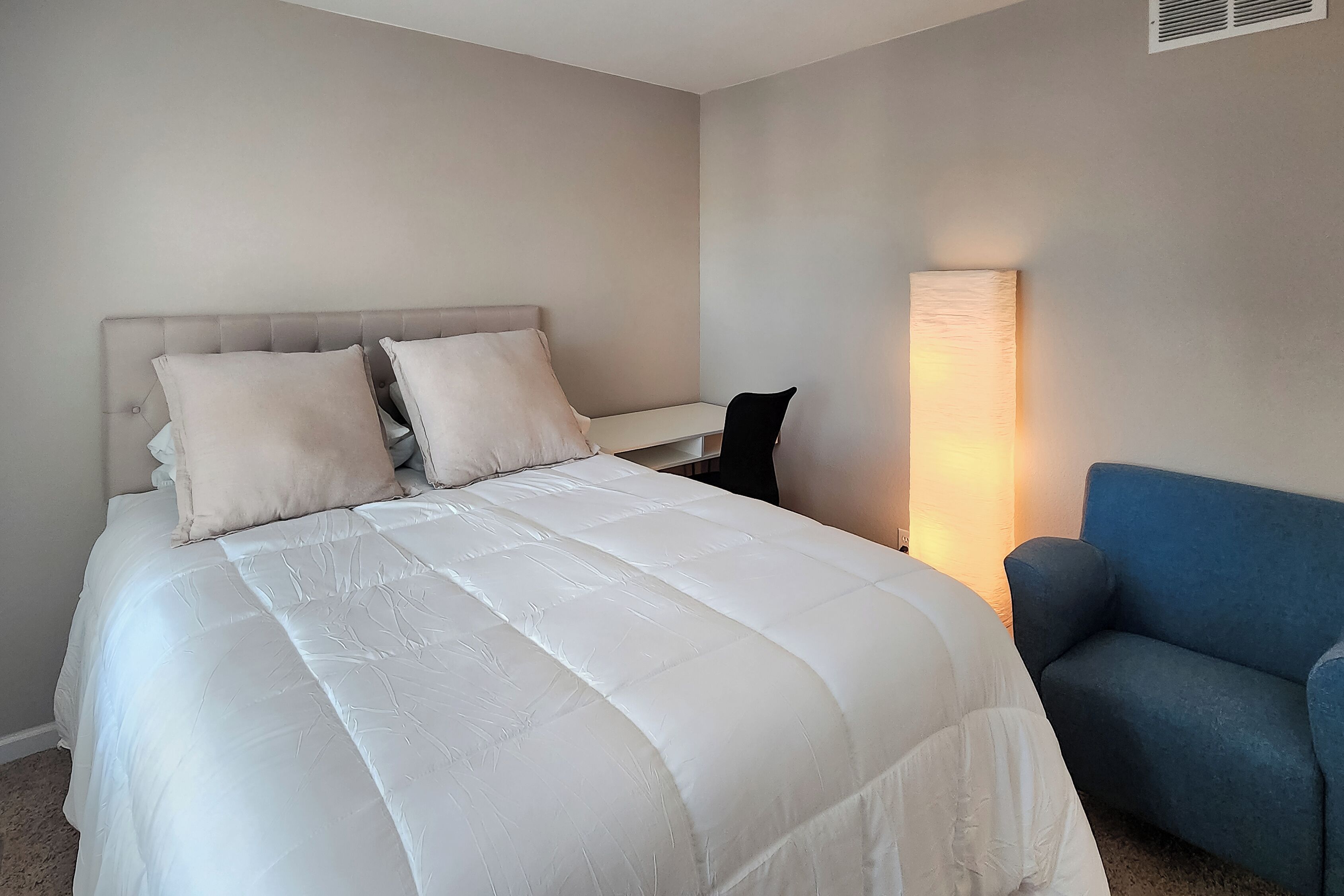 Een slaapkamer met een bed, een stoel en een nachtkastje.