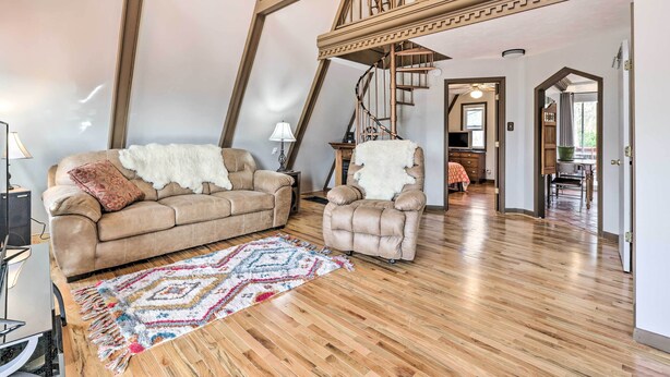 A spacious loft with a high ceiling, exposed wooden beams, a spiral staircase, a plush beige sofa, a matching armchair, and a colorful rug. - Peaceful Mt Sterling Cabin: Deck & Fire Pit! (Mt Sterling)