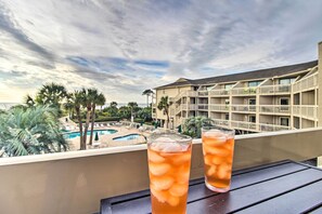 Dos vasos de té helado en un balcón con vista a una piscina y un edificio de hotel.