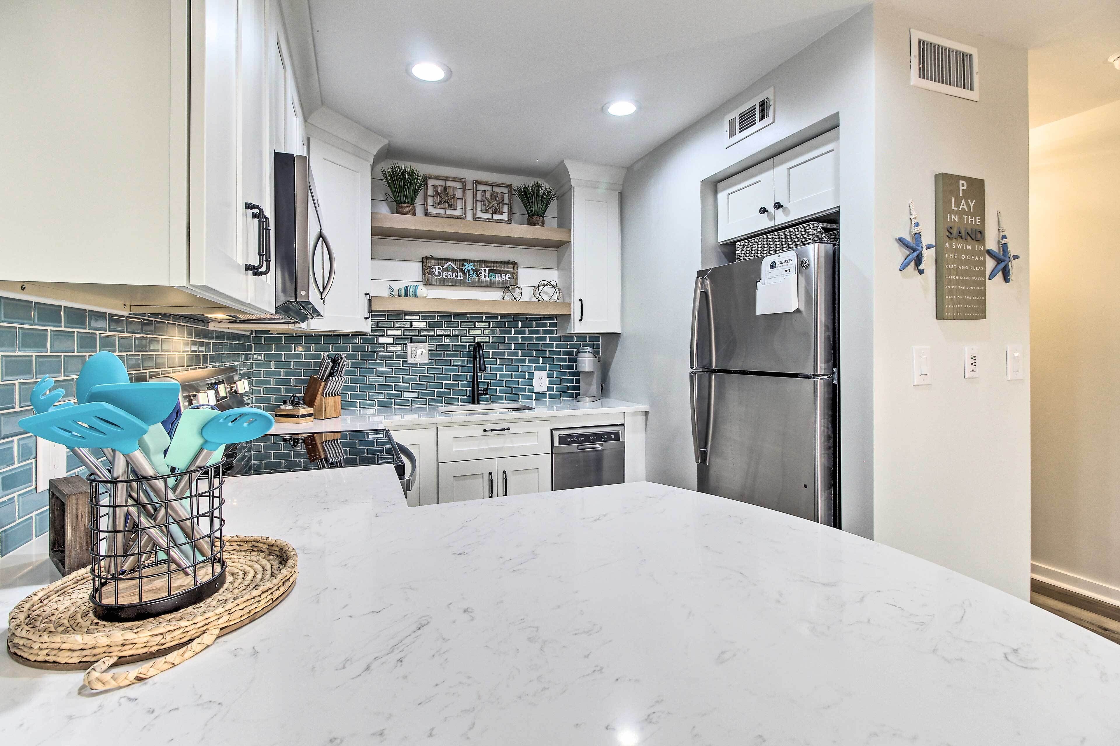 A modern kitchen with white cabinets, a marble countertop, and a stainless steel refrigerator.