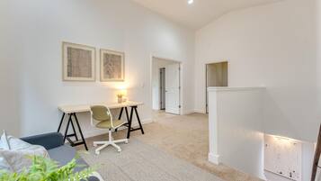 Un salon moderne avec un bureau, un canapé confortable et une petite plante. Deux tableaux encadrés ornent le mur, et une porte donne accès à une autre pièce.