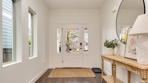 Un couloir avec un plancher en bois, une porte blanche et une console sur laquelle sont posés une lampe et un tableau encadré.