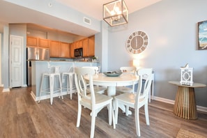 A modern kitchen with wooden cabinets, a stainless steel refrigerator, and a dining area with white chairs and a round table. - Beachy Condo w/ Lagoon-Style Pool Views at The Palms of Destin! πβπ΄ (Destin)