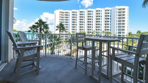A balcony with white chairs and a table, overlooking a pool and a building with multiple balconies. - Beachy Condo w/ Lagoon-Style Pool Views at The Palms of Destin! 💚☀🌴 (Destin)