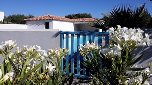 A white building with a red-tiled roof, a blue gate, and white flowers in the foreground. - Elaia Silvis on the Mediterranean – 14-meter heated pool (TOUROUZELLE 11200)